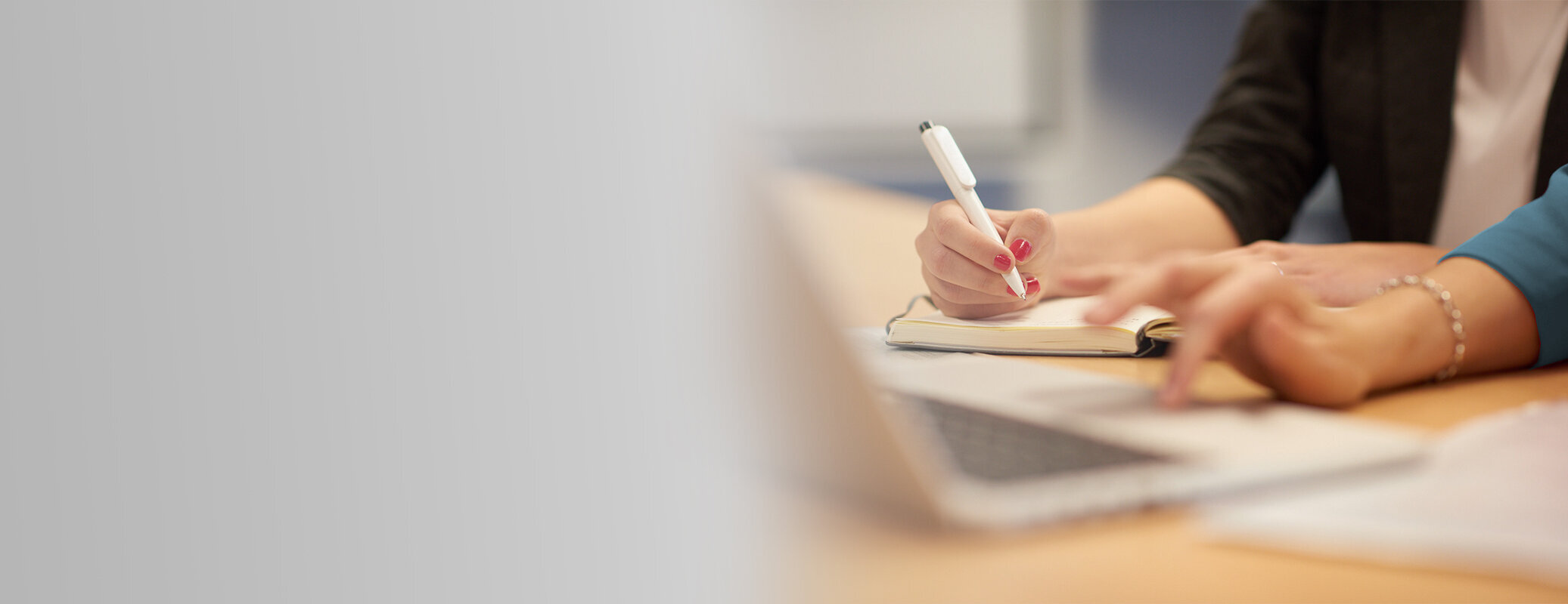 Two people working together at a desk, writing notes and using a laptop.