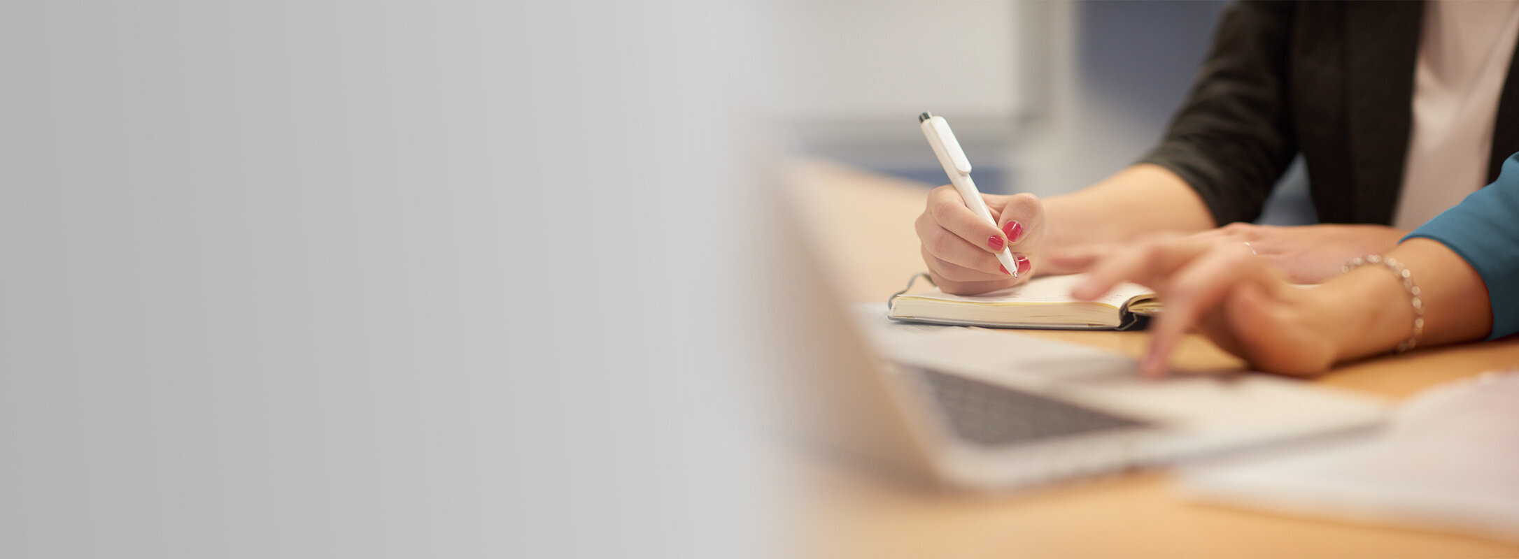 Two people working together at a desk, writing notes and using a laptop.